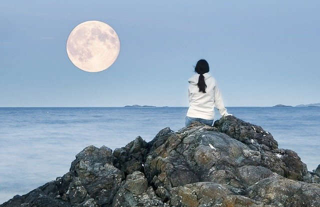 Girl or Woman gazing at the full moon over the ocean
