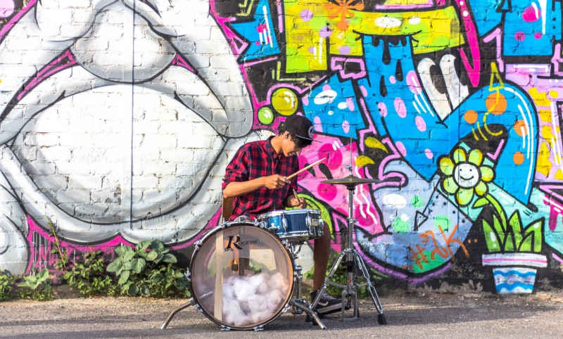 Man playing drum set in front of mural.